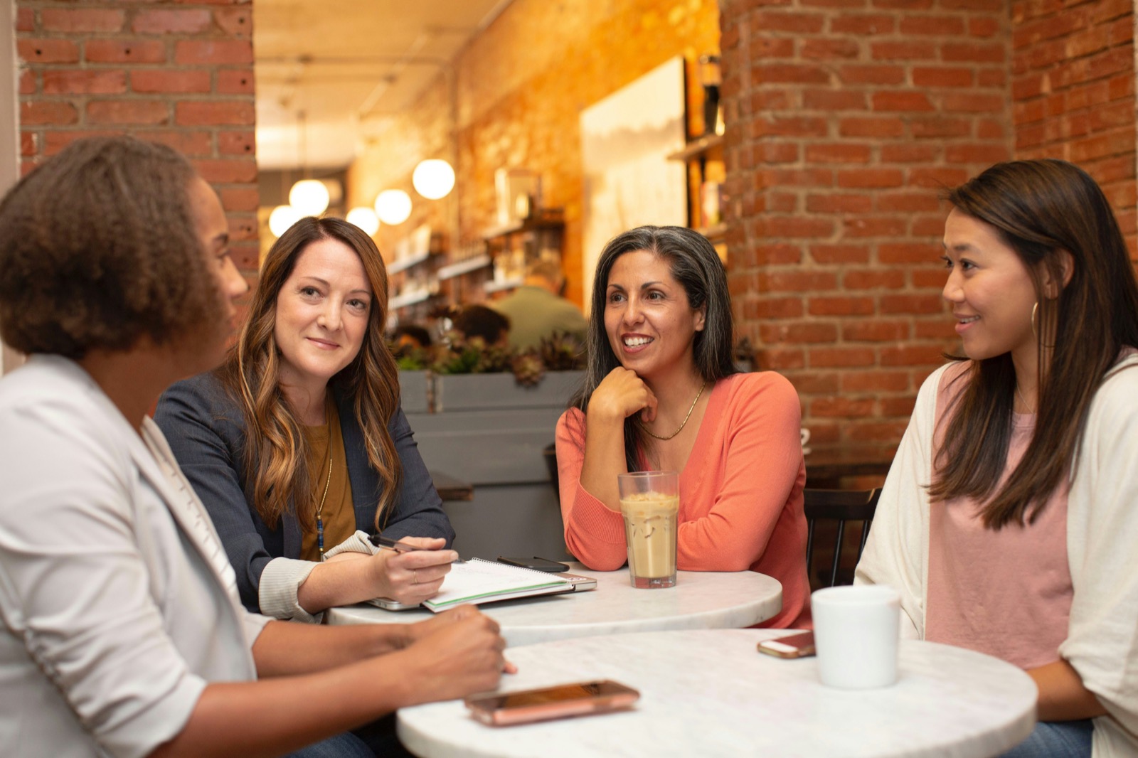 Four women talking round a café table, one of them smiling and resting her chin on her hand