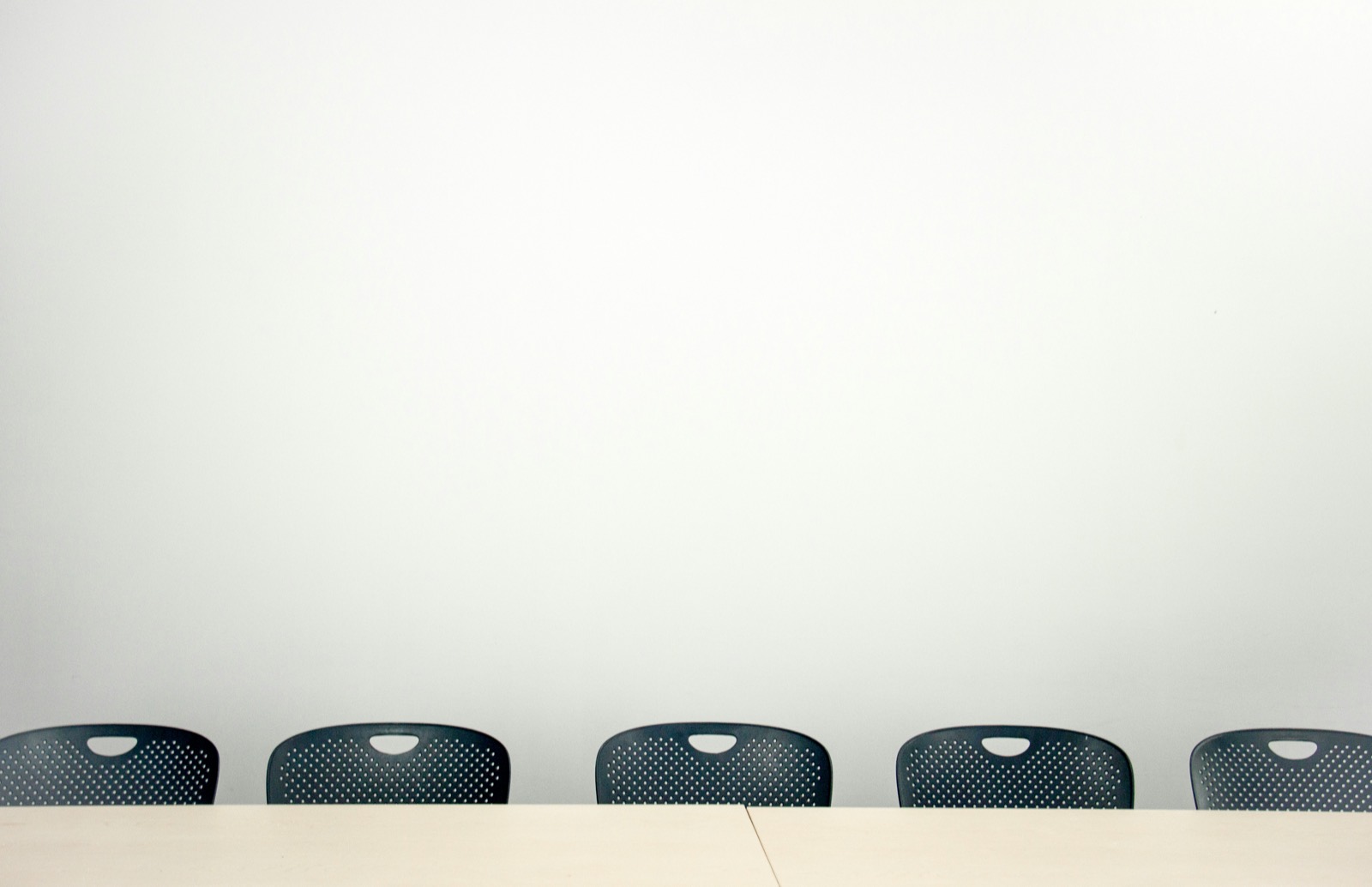 A row of empty chairs along a table against a plain white wall